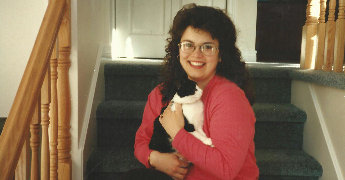 The late Darla Nault sits on the stairs, wearing a pink sweater and holding a cat