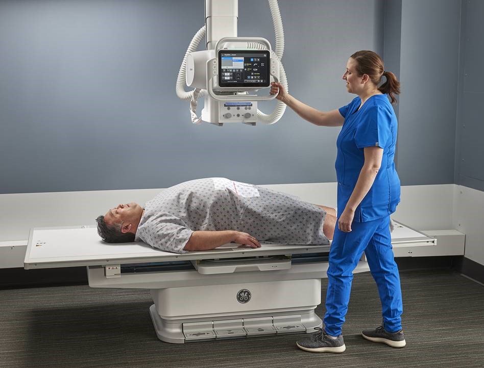 A male patient prepares for an x-ray with a female clinician operating the machine. 