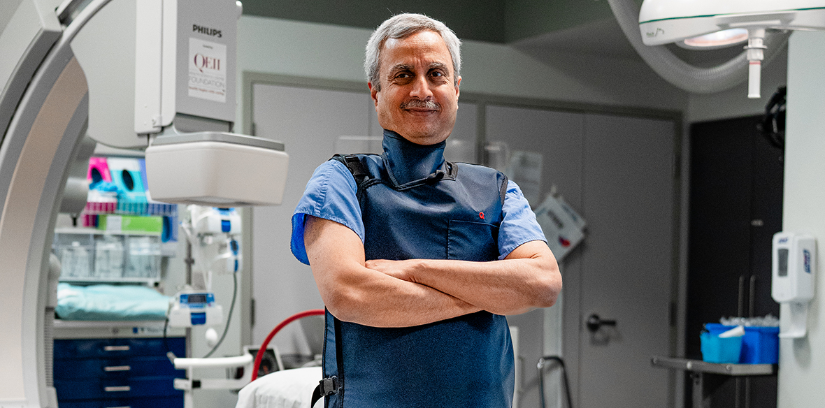 Dr. Quraishi stands with crossed arms in front of a medical background. 
