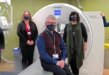 Five healthcare professionals wearing masks stand in front of the QEII's PET-CT scanner