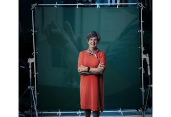 A woman in a red dress stands in front of a green screen with a healthcare image behind her