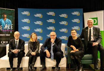 Five people wearing business attire sitting on a stage and smiling at the camera.