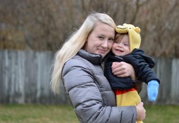 A woman holding a toddler in her arms. Both of them are smiling at the camera. 