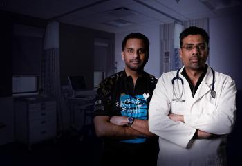 Two males looking towards the camera with slight smiles. The male on the left wears a cycling jersey. The male on the right is in a white coat and stethoscope around his neck.