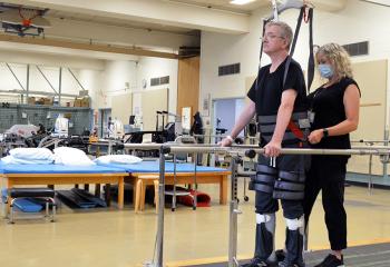 Barry Pettipas stands in the body weight support system with the help of a QEII physiotherapist