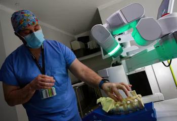 Surgeon in blue scrubs stands in front of glowing robot