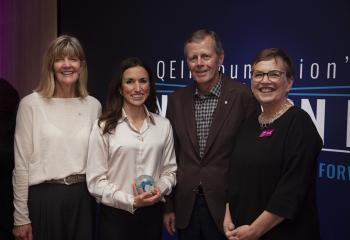 Three women and a man standing together for a photo, smiling at the camera. 