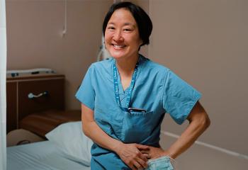 Physician wearing blue scrubs, standing in patient care area