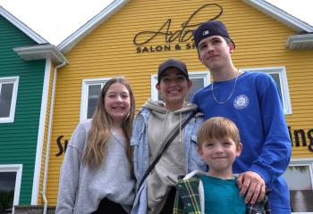 A woman and three children smile at the camera with brightly coloured buildings behind them. 