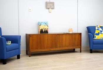 Two blue chairs with decorative pillows and a cabinet with a salt lamp sit in a bright room