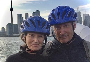 A couple wearing bicycle helmets pose in front of the Toronto skyline.