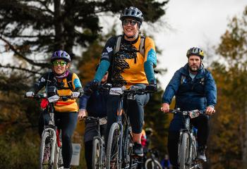 Three people dressed in BMO Ride for cancer jerseys ride there bikes on the trail during the 2025 event.