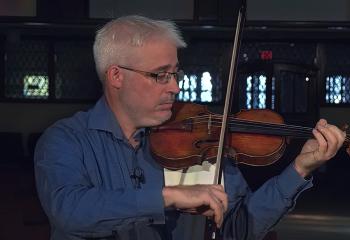 Renaud plays a violin with a church background. 