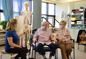 A QEII physiotherapist uses an anatomical skeleton to show a patient and his wife the site of is injury.