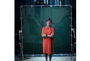 A woman in a red dress stands in front of a green screen with a health care image.