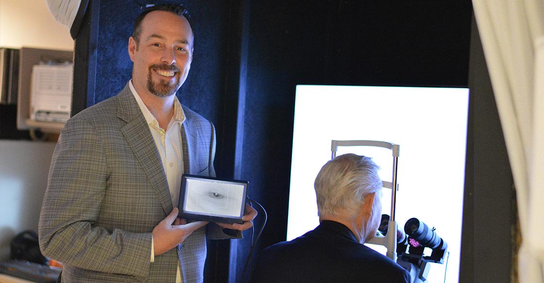 Charles Rutt looks into the glaucoma detection device, Dr. Brennan Eadie displays the image of Charles’ eye on a hand-held screen.