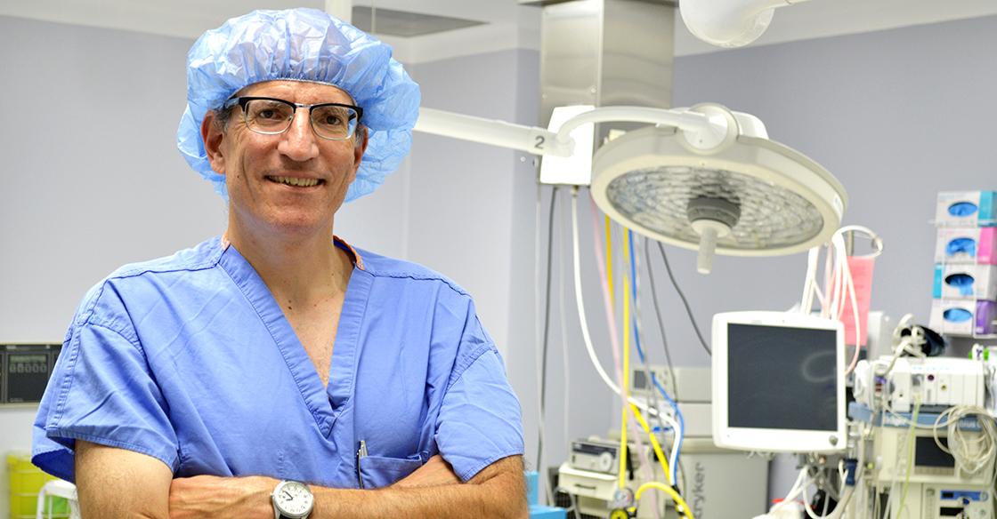 Dr. Hirsch stands in his blue scrubs in front of medical equipment