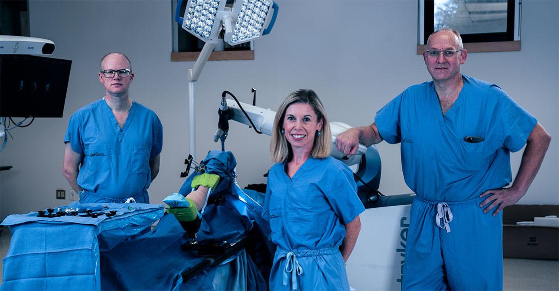 Dr. Glen Richardson, Janie Wilson, PhD and Dr. Michael Dunbar stand with the Mako orthopaedic surgical robot.