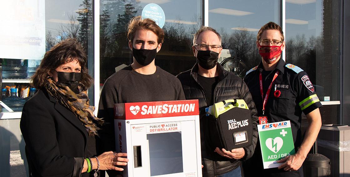Debbie Boyd, Bronson Beaton, Stephen Boyd and Mike Janczyszyn stand outside of the Oxford Irving, holding a donated automated external defibrillator.