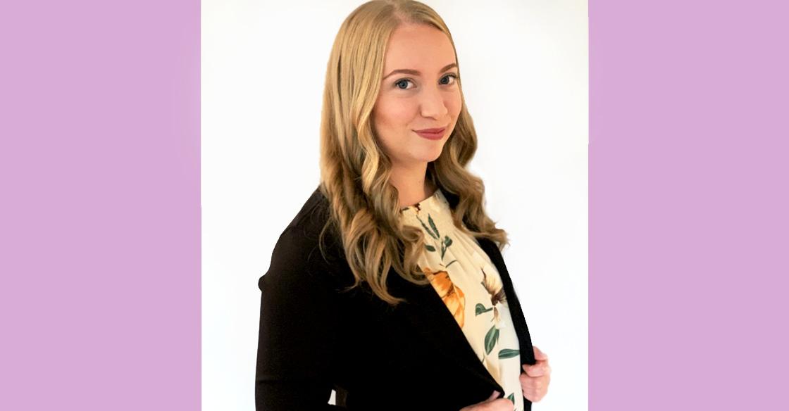 Kayla Ross poses for a photo wearing a black jacket and floral shirt