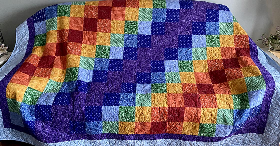 A large rainbow coloured quilt adorned with a hand-stitched rose pattern