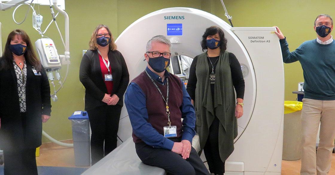 Five healthcare professionals wearing masks stand in front of the QEII's PET-CT scanner