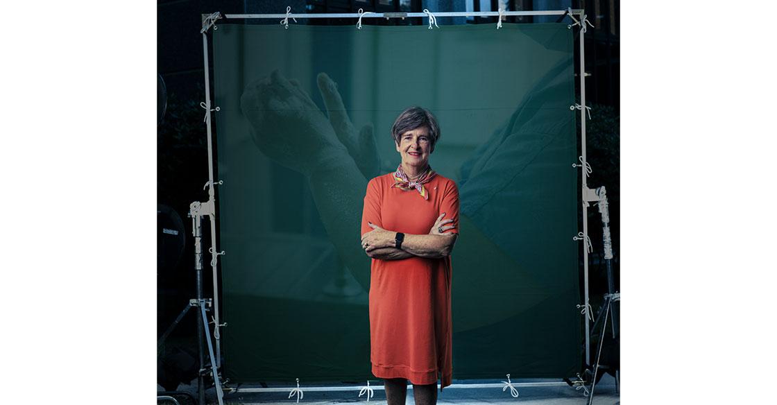A woman in a red dress stands in front of a green screen with a healthcare image behind her