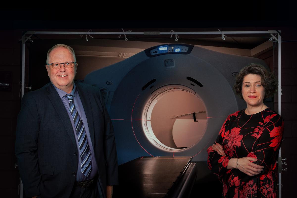 Two cancer care experts stand in front of the QEII's CT simulator machine, which resembles a CT scanner