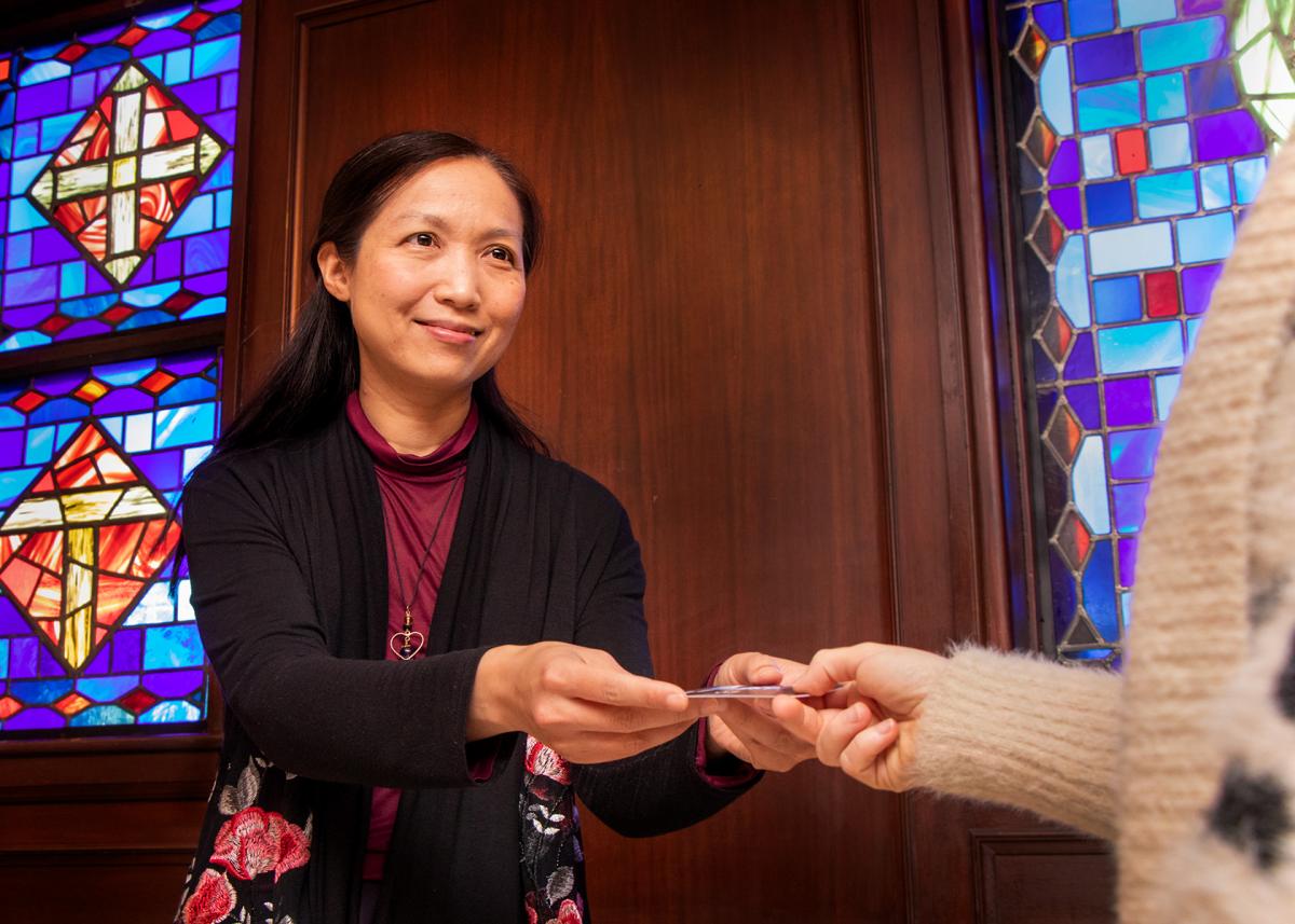 A woman, smiling, extends a gift card to another person, whose hand is reaching out. Their face is not shown. 