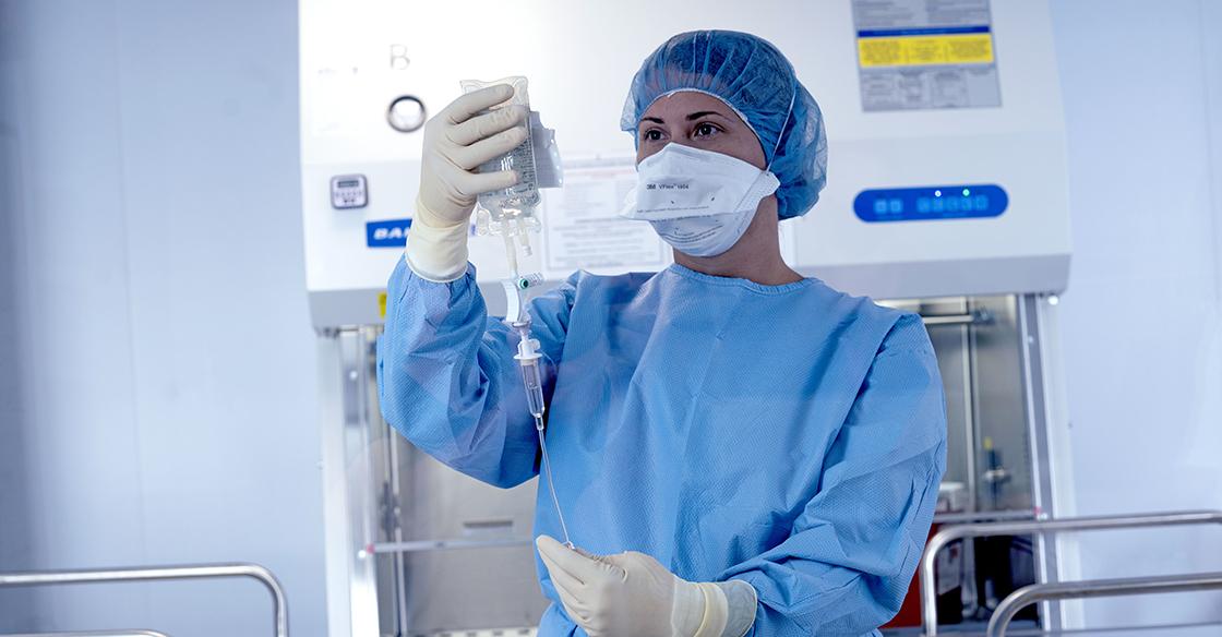 A woman dressed in blue scrubs holds up a medical vial