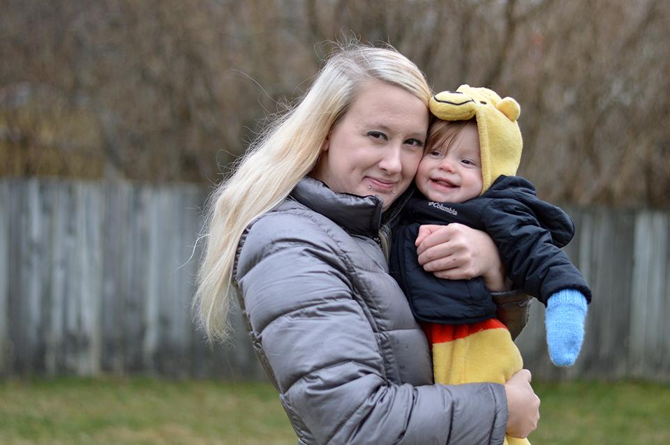 A woman holding a toddler in her arms. Both of them are smiling at the camera.