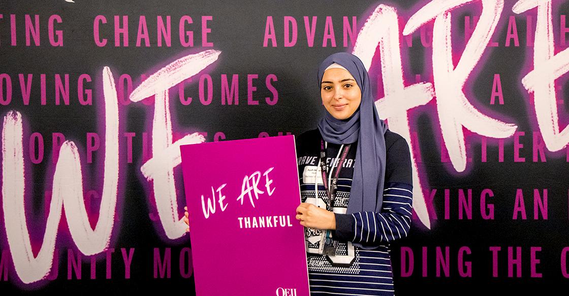 Ayah holding a sign in front of a celebration backdrop