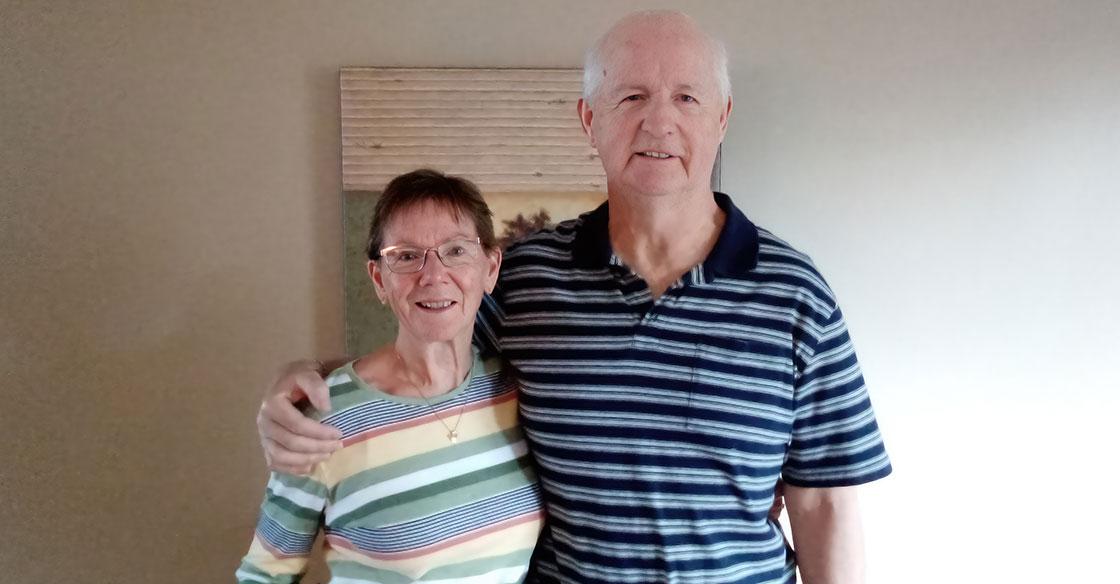 Older couple stands in front of beige wall and painting