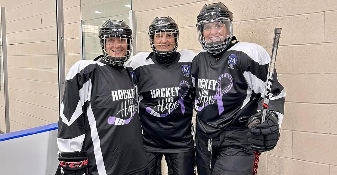 Three women standing together, wearing hockey gear