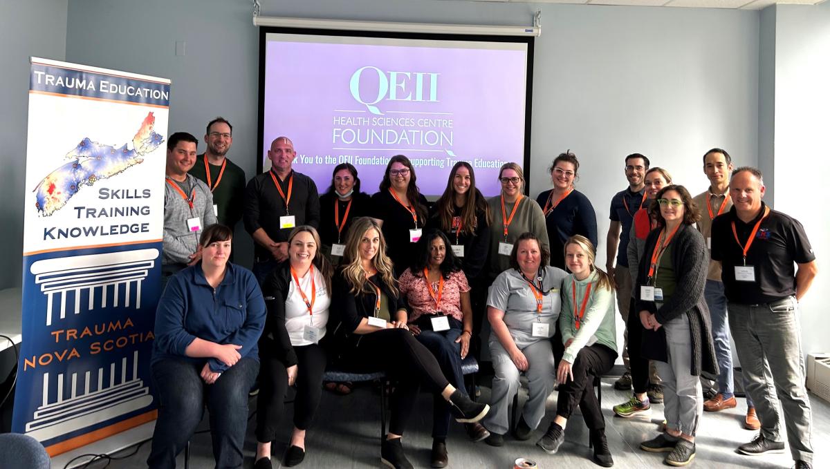 A group of people are posed smiling and facing the camera. A screen is behind them with the QE 2 Foundation logo. 