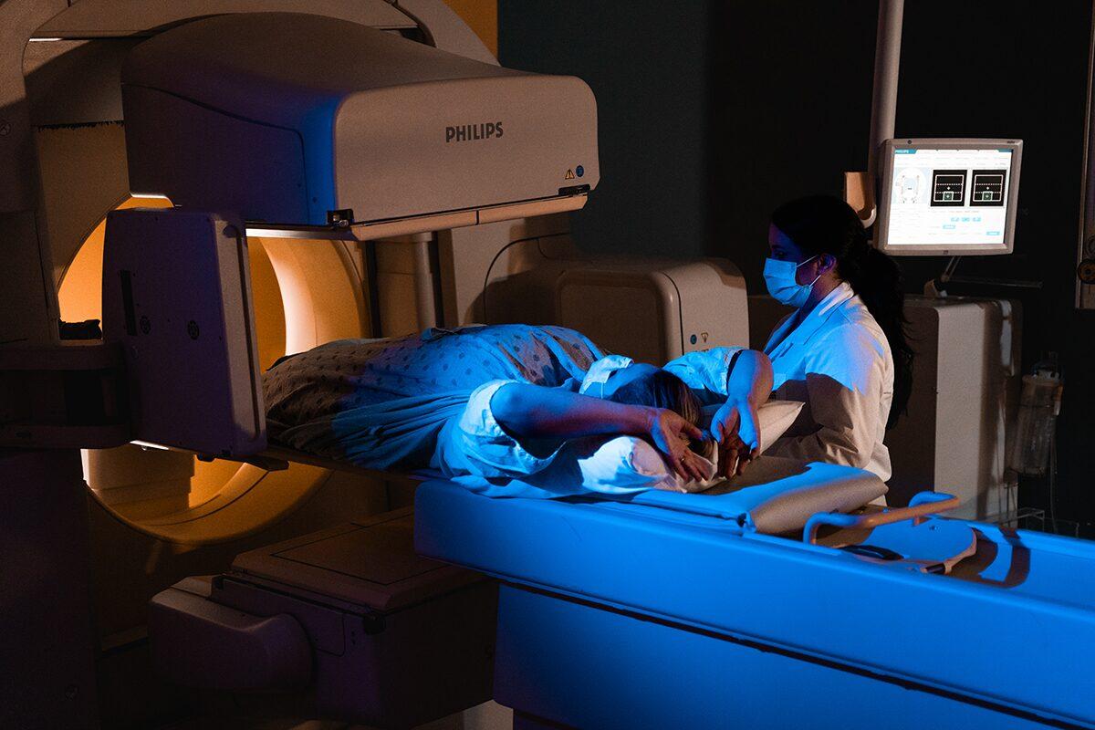 A person lies in a medical scanner, with a healthcare provider to the right of the scanner preparing the patient for the procedure.