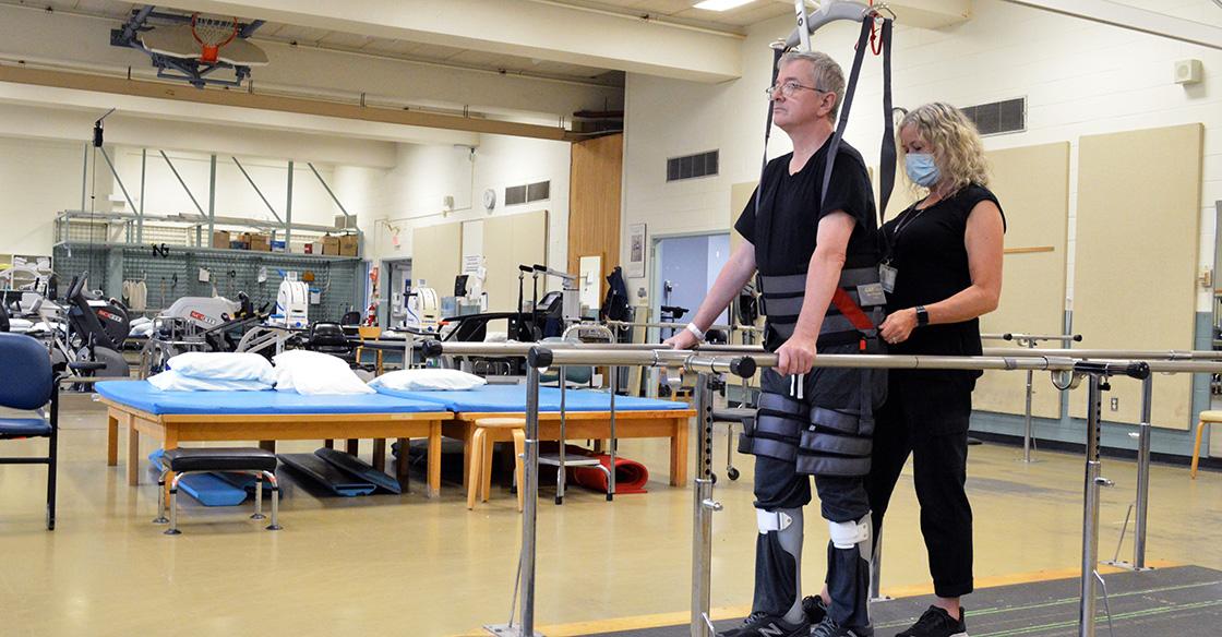 Barry Pettipas stands in the body weight support system with the help of a QEII physiotherapist