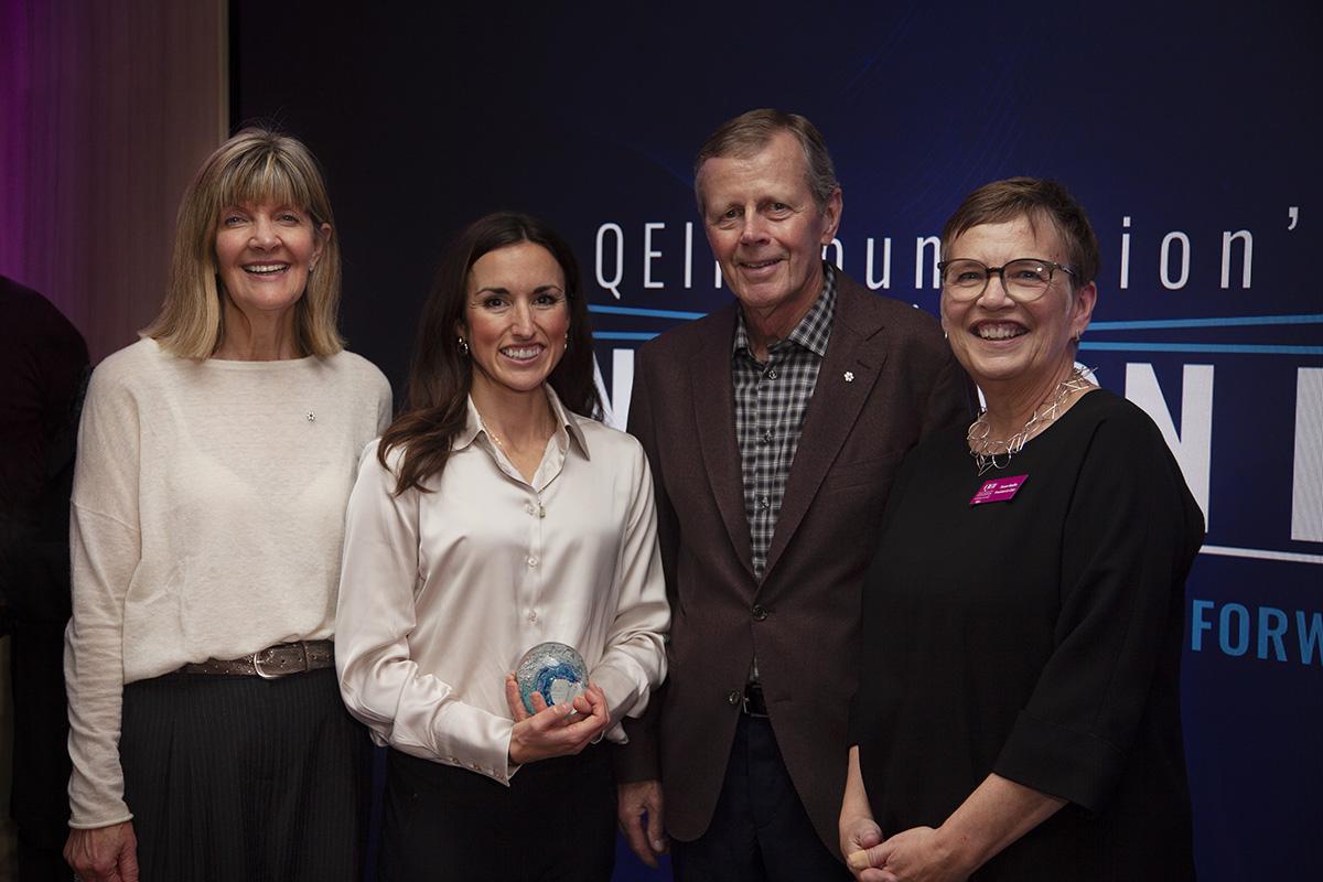 Three women and a man standing together for a photo, smiling at the camera. 