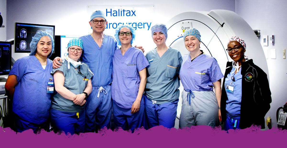 A group of doctors in an operating room, wearing scrubs and smiling at the camera.