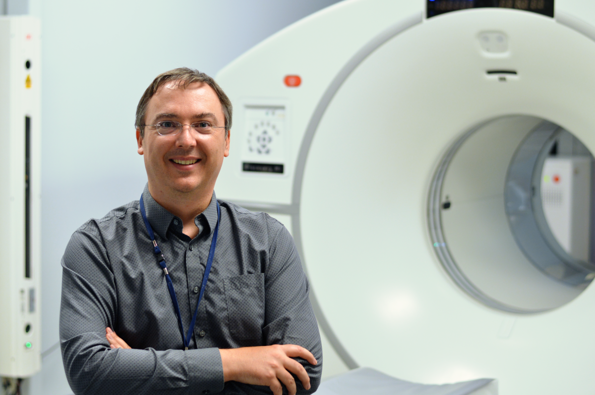 A man stands in front of a diagnostic imaging machine in a healthcare setting. 