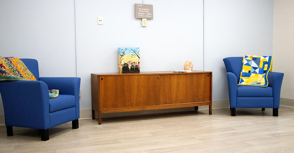 Two blue chairs with decorative pillows and a cabinet with a salt lamp sit in a bright room