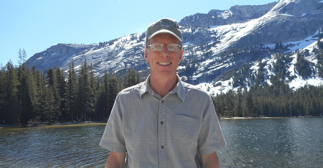 Rob stands in front of lake with mountains in backgroudn