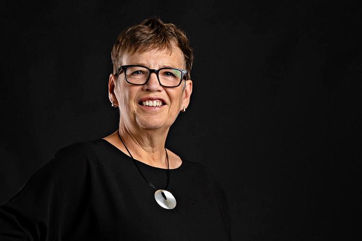 Susan Mullin, CEO at the QEII Foundation, poses for the camera on a dark background.