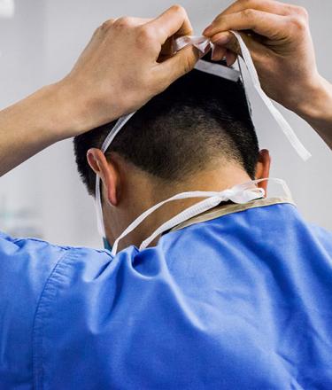 A doctor ties his mask and prepares for surgery