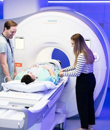 A patient is receiving an MRI scan under the watch of two healthcare professionals.