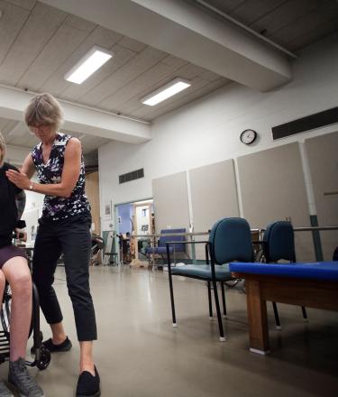 A woman in a wheelchair receives assistance from a physical therapist. 