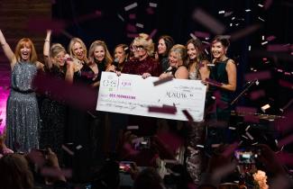 On-statge cheque presentation photo with confetti and celebrating more than $1.2M raised