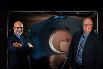 Two cancer care experts stand in front of the QEII's CT simulator machine, which resembles a CT scanner