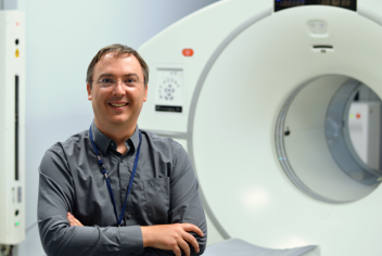 A man stands in front of a diagnostic imaging machine in a healthcare setting. 