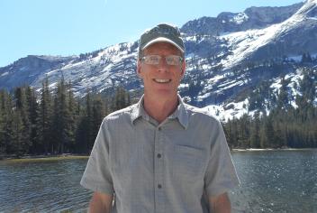 Rob stands in front of lake with mountains in backgroudn